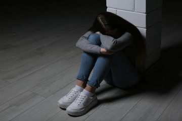 Upset teenage girl sitting at column indoors. Space for text