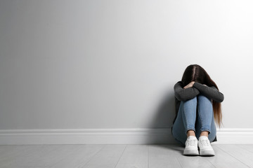 Upset teenage girl sitting on floor near wall. Space for text