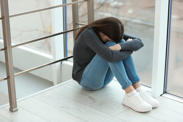 Upset teenage girl sitting at window indoors