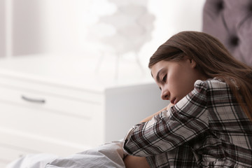 Upset teenage girl sitting on bed. Space for text