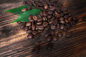 Brown arabica coffee beans with leaf on a wooden board.