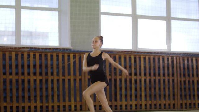 Young girl in sportswear performing jumps with front splits when having rhythmic gymnastics class
