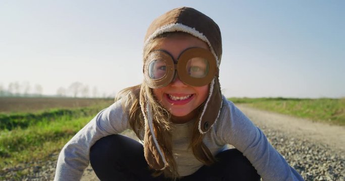 Authentic shot of cute little girl with aviator hat having fun and smiling in camera on a spring nature background in a  sunny day.