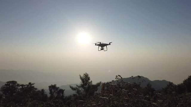 4K Viseo Selective focus low angle tracking shot white drone with camera flying over mountain peak against sunlight in morning sunrise sky .