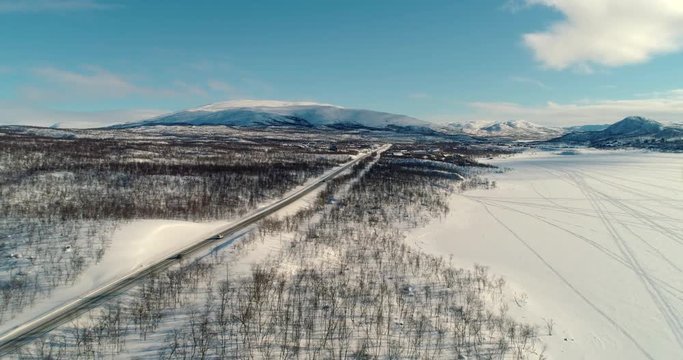 Car in a arctic town, C4k aerial, drone shot, following a car driving towards a north scandinavian village, on a sunny, winter day, in Kilpisjarvi, Enontekio, Lapland, Finland