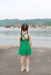 Rear view of little Asian kid girl standing in hillside near resort.