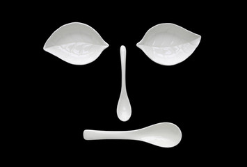 Funny face from white ceramic leaf bowl and spoon isolated on black background.