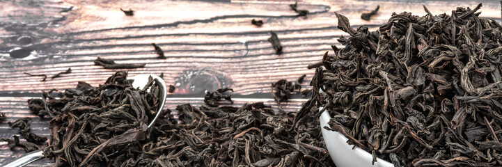 Dried tea is poured into a ceramic cup on a wooden plank table.