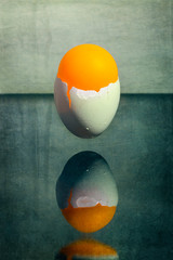 Eggshell stuck in the air above the table with an orange ball, surreal still life "Morning"
