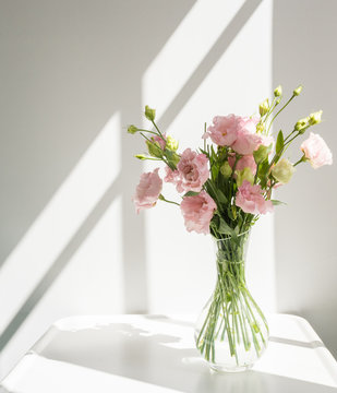 Close Up Of Pink Lisianthus  Flowers In Glass Vase On White Table With Bright Sunlight And Hard Shadows From Window