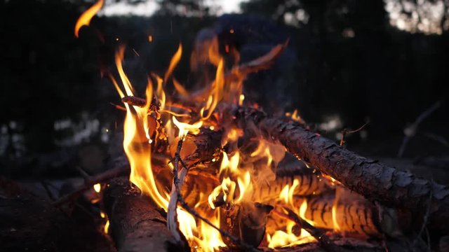 Camp fire embers floating into evening sky slow motion tilt up, close up