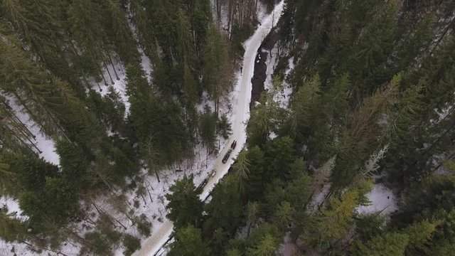 Three horse teams ride a narrow mountain valley next to a stream during late winter.