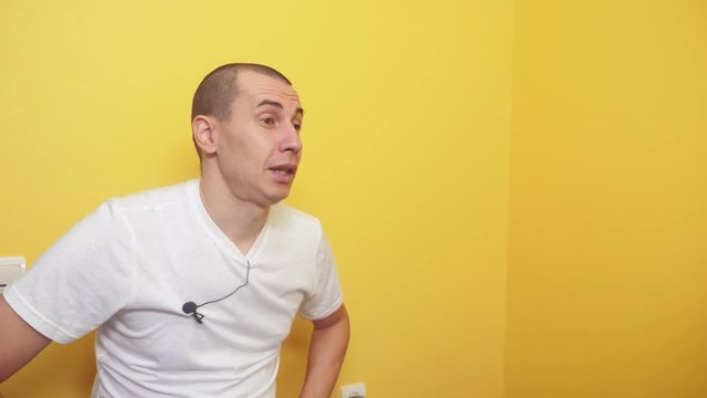 blogger man concept. male recording video with microphone buttonhole on t-shirt against yellow wall background lifestyle. man talking blogger