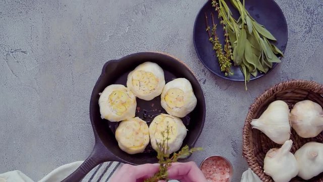 Raw garlic heads with fresh spices in cast iron skillet for preparing roasted garlic recipe.