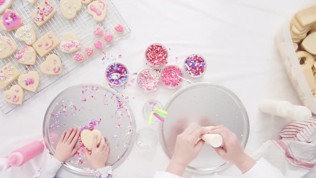Flat lay. Step by step. Little girl decorating decorating sugar cookies with royal icing and sprinkles for Valentine's Day.
