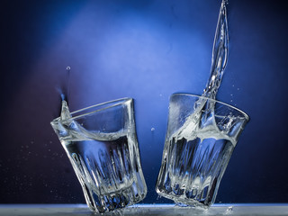 Falling and jumping glass with spilling liquid on a blue gradient background