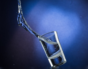 Falling and jumping glass with spilling liquid on a blue gradient background