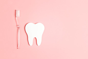 White paper tooth with toothbrush on pink background. Dental health concept. Flat lay, top view,...