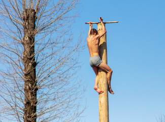 A man climbs a wooden pole against the blue sky