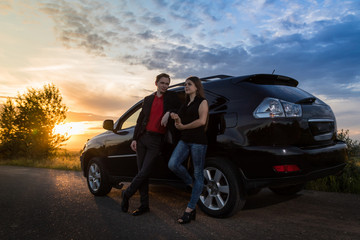 Couple standing near the car in a summer evening