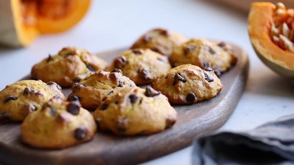 Hands put a wooden tray with pumpkin cookies with chocolate chips on a table.