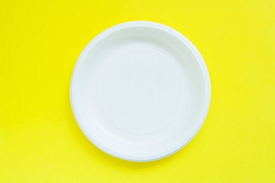 Disposable Plastic Plates On Bright Yellow Background With Copy Space.