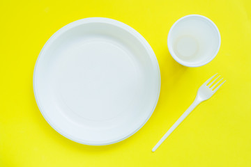 Disposable plastic tableware on bright yellow background with copy space.