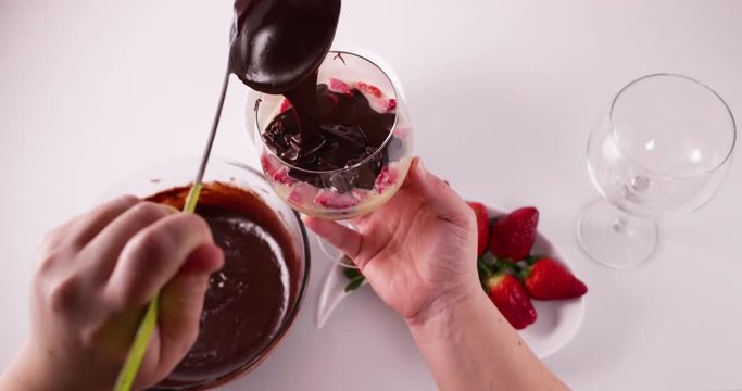 Speed up clip of Lady pouring melted chocolate from a cream spoon into a glass with a mixture of condensed milk, cream, and strawberries to prepare a pave french dessert recipe 4K 30 fps