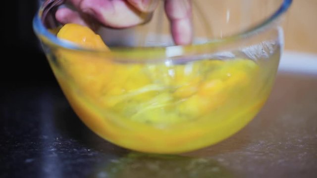 Lady stirring eggs in a clear glass bowl with a stainless still stirrer as a preparation for a delicious ham cheese and mushroom omelet 1080p 30 fps