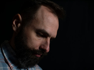 Closeup face of a stylish man with a beard and mustache with a serious face looking down on a black background
