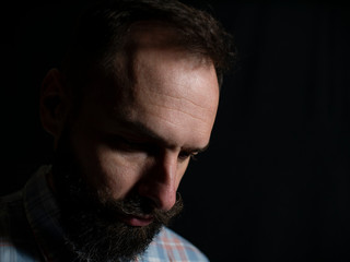 Closeup face of a stylish man with a beard and mustache with a serious face looking down on a black background