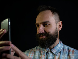 Attractive man with a beard and mustache carefully looks at the phone on a black background