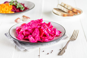 Canned fermented purple cabbage with beets, carrots and garlic on a white plate,on a white napkin,on a light natural table, in a horizontal orientation.