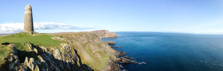 A large rock tower sits on a grassy field at the tip of the Oa Peninsula on the island of Islay in Scotland.