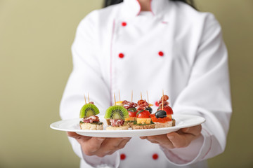 Chef holding plate with tasty canapes on color background