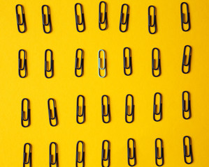 White paper clip among black ones on color background. Concept of uniqueness