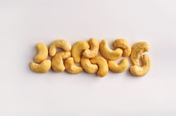 A horizontal row of dry raw cashew nuts on a studio white background.