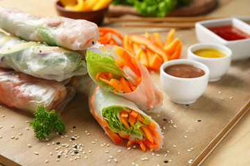 Tasty spring rolls with sauces on wooden board