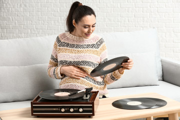 Pregnant woman listening to music through record player at home