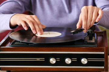 Young woman listening to music through record player at home, closeup