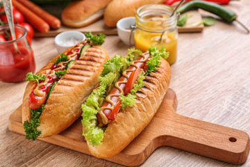 Board with tasty hot dogs on table