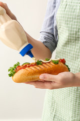 Woman pouring tasty hot dog with sauce on white background