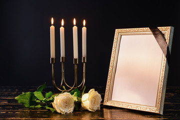Blank funeral frame, candles and flowers on table against black background
