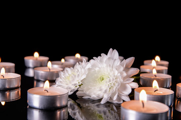 Many burning candles as symbol of mourning and flowers on dark background