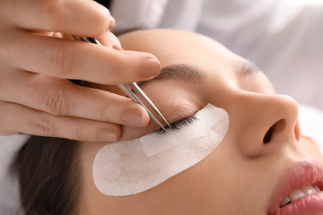 Naklejka premium Young woman undergoing eyelash extension procedure in beauty salon, closeup