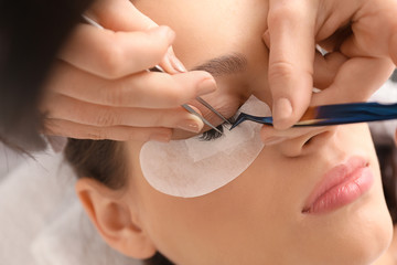 Obraz na płótnie Canvas Young woman undergoing eyelash extension procedure in beauty salon, closeup