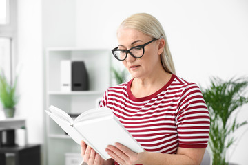 Mature woman with hearing aid reading book at home