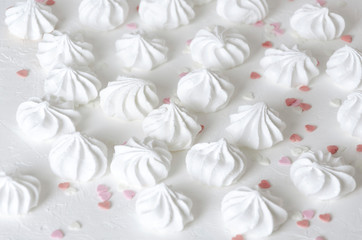 Heart sprinkles and little fresh baked meringues on white surface