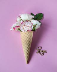 Ice cream horn or cone with roses on a pink background and Love word. Happy Mother's Day, Women's Day or Birthday. Floral flat lay minimalism,  greeting card. Top view. Copy space. Selective focus.
