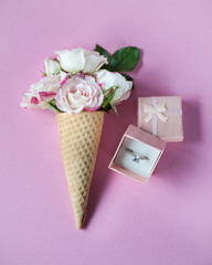 Box with engagement ring on a pink background with coral roses. Floral flat lay minimalism,  greeting card. Wedding concept. Top view. Copy space. Selective focus. Close-up.